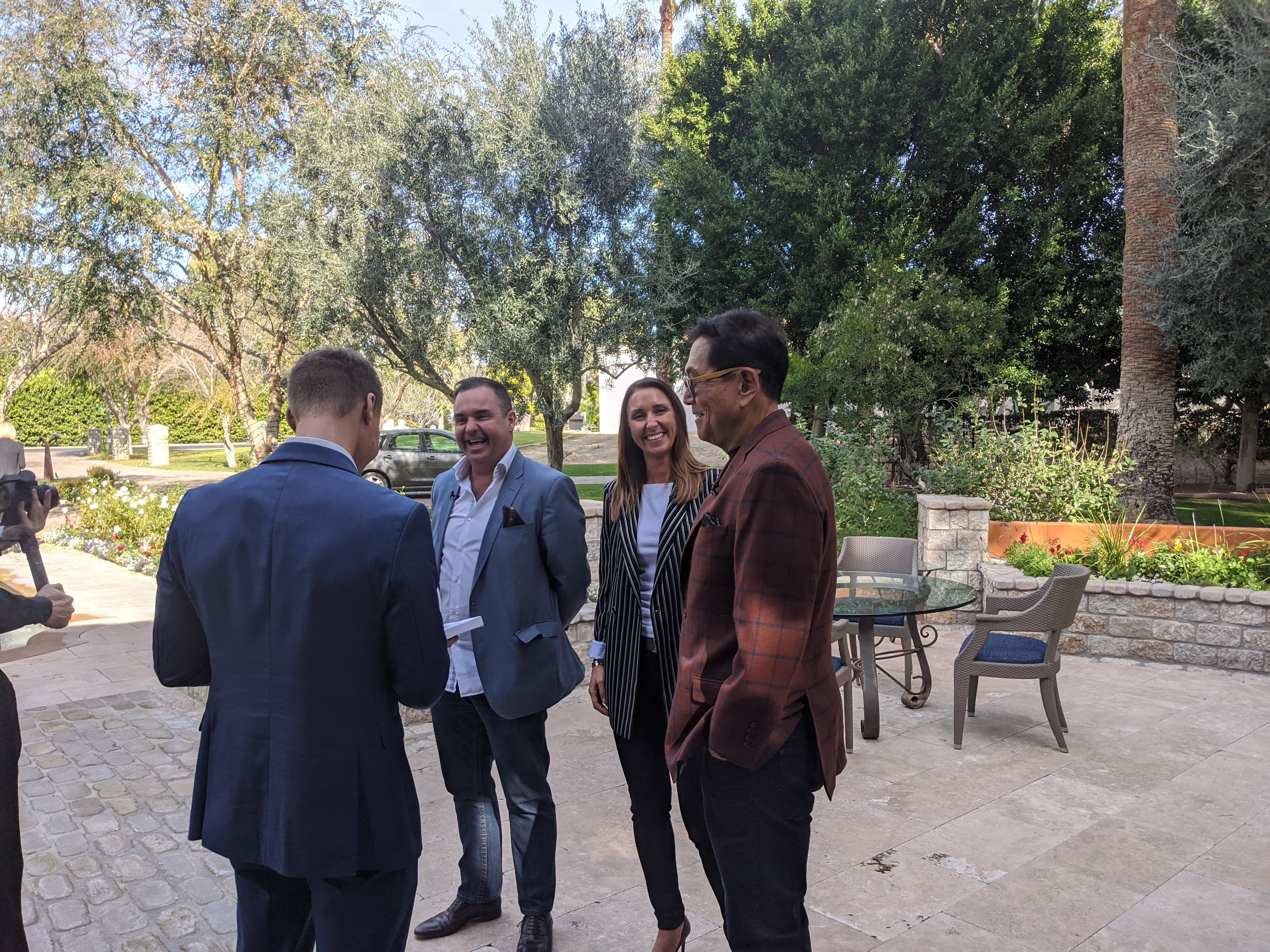 Four people in business attire smile and talk on a sunny outdoor stone patio.